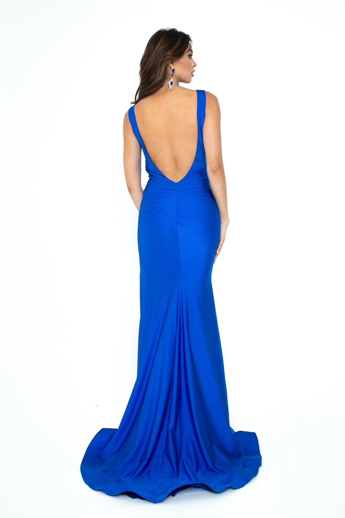 A woman faces away, wearing the Open-Back Sleeveless Long Prom Dress: Atria 6306H in royal blue, featuring a deep V-back and mermaid silhouette, against a white background.